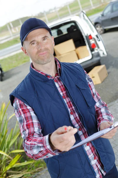 Zusteller schreibt auf Klemmbrett vor seinem Lieferwagen — Stockfoto