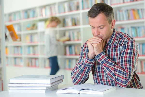 Man zat leest aan tafel in bibliotheek — Stockfoto