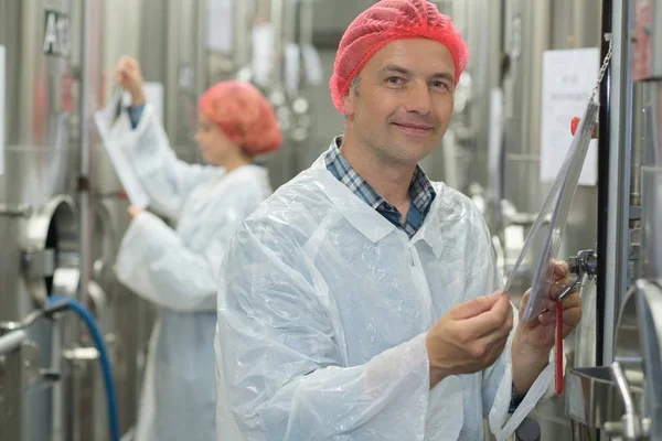 Ein fröhlicher Mann in Uniform steht inmitten einer Brauerei-Edelstahlanlage — Stockfoto