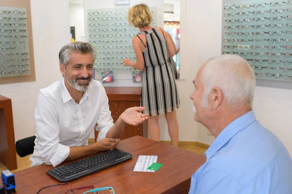 Профессиональный мужчина-оптик консультирует пожилого клиента — стоковое фото
