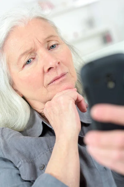 Пожилая женщина со смартфоном смс-кой дома — стоковое фото