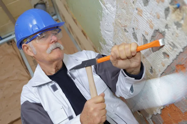 Senior builder använder en hammare för att ta bort väggar gips — Stockfoto