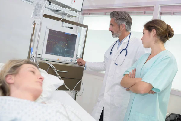 Kvinnlig patient i sängen medan läkarna tittar på röntgen — Stockfoto