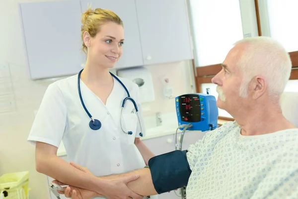 Junge Ärztin überprüft Blutdruck eines älteren männlichen Patienten — Stockfoto