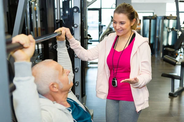 Instrutor de fitness ajudando o homem idoso usando pesos — Fotografia de Stock