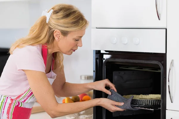 Mooie blonde vrouw zetten taart in de oven voor het bakken — Stockfoto