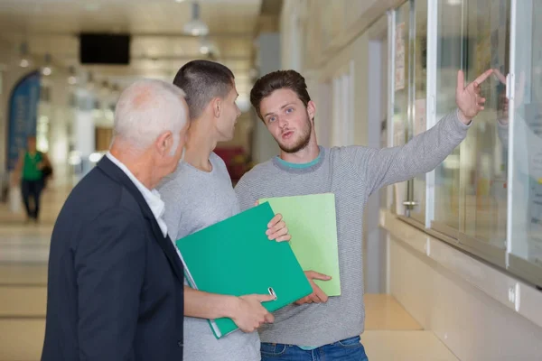 Profesor z notatnikiem rozmawiający z uczniem na korytarzu — Zdjęcie stockowe