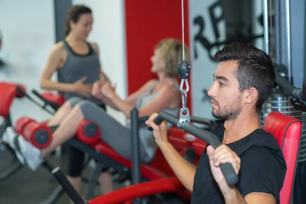 Hombre joven está levantando peso mientras hace ejercicio en el gimnasio —  Fotos de Stock