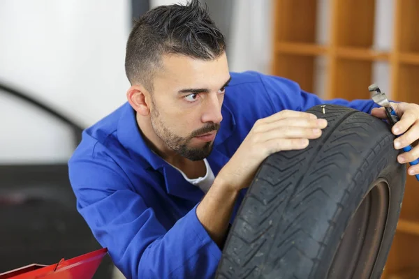 Jeune mécanicien en uniforme avec pneu — Photo