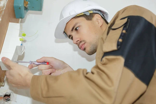 Construtor com chave de fenda fixação tomada dentro de casa — Fotografia de Stock