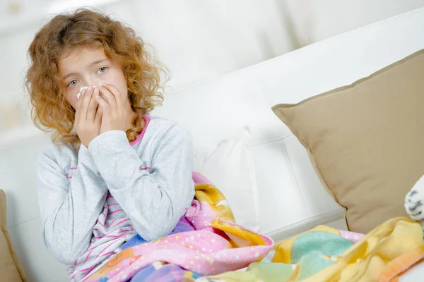 Young girl sat on couch, blowing nose — Stock Photo, Image