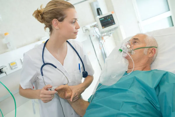 Женщина-врач смотрит на пожилого пациента в кислородной маске — стоковое фото