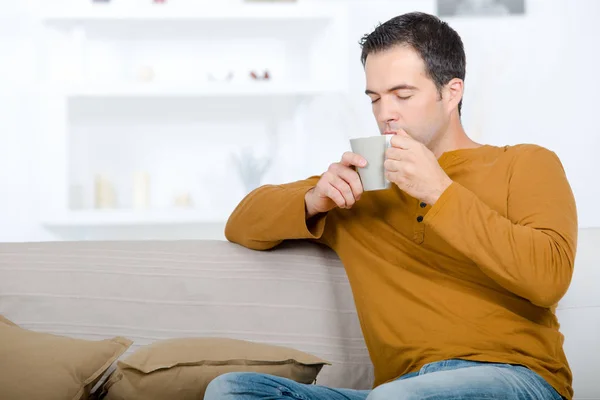 Мужчина сидел на диване, наслаждаясь горячим напитком — стоковое фото