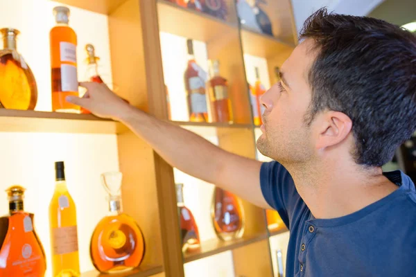 棚からブランデーのボトルを選択する男 — ストック写真