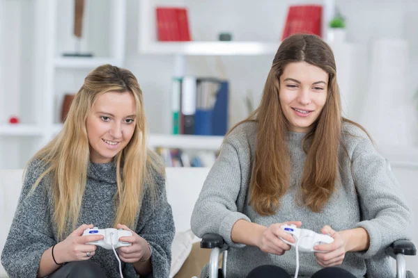 Amigos do sexo feminino jogando videogames em casa um em cadeira de rodas — Fotografia de Stock
