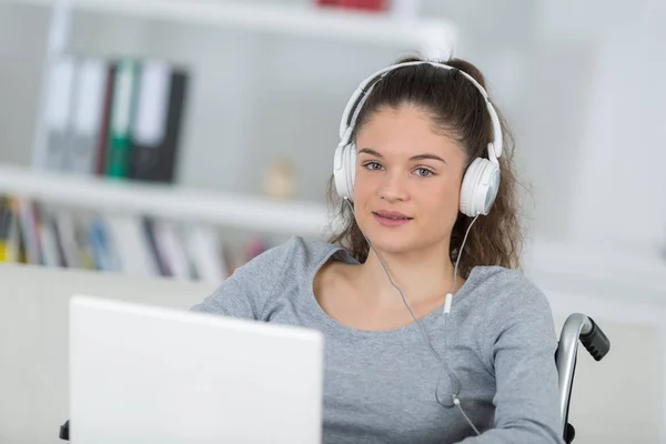 Tonårsflicka i rullstol bär hörlurar och använder bärbar dator — Stockfoto