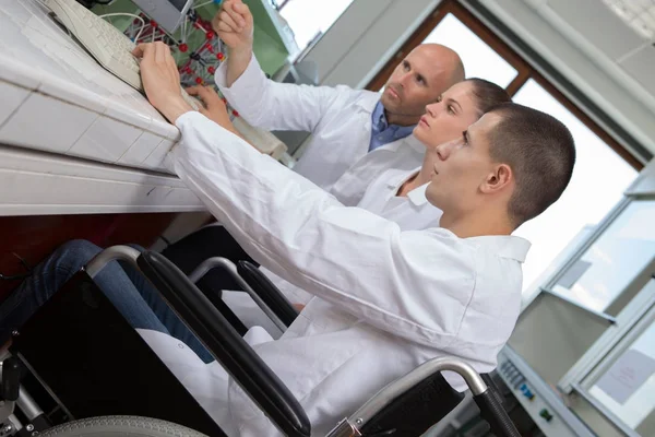 Νεαρός άνδρας σε αναπηρικό καροτσάκι και γυναίκα στο εργαστήριο — Φωτογραφία Αρχείου
