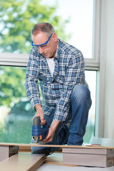 Hombre carpintero constructor que trabaja con rompecabezas eléctrico y madera — Foto de Stock