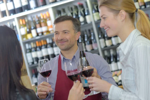 Jonge mensen het roosteren van rode wijn met handelaar in kelder — Stockfoto