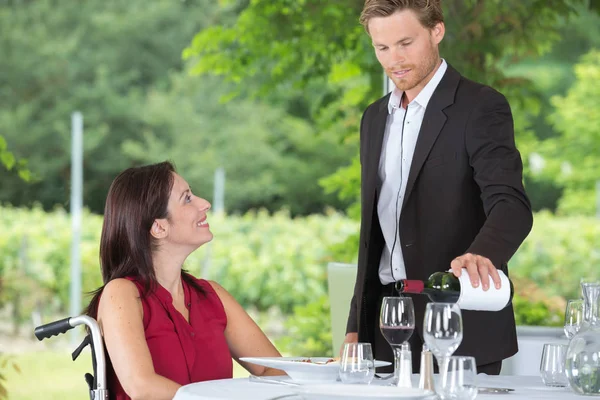 Smiling woman in a wheelchair talking to waiter — Stock Photo, Image