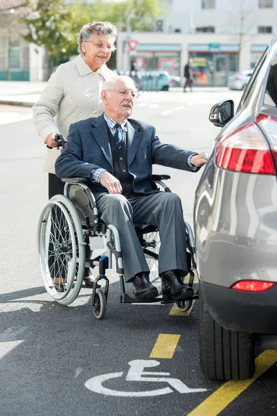 Femme poussant son mari handicapé vers la voiture — Photo