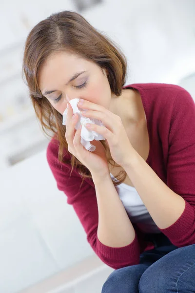 Больная молодая женщина чихает в салфетке — стоковое фото