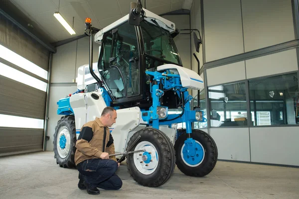 Joven trabajador chequeando tractor viñedo en el garaje — Foto de Stock