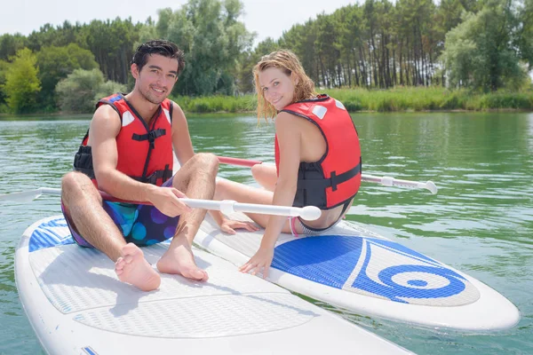 Man and woman sat on boards in river — Stock Photo, Image