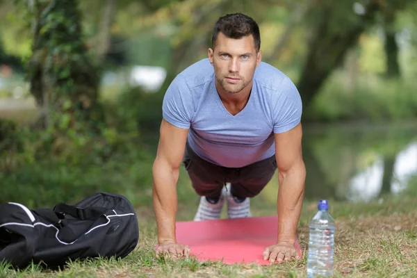 Jovem muscular fazendo flexões no parque no gramado — Fotografia de Stock