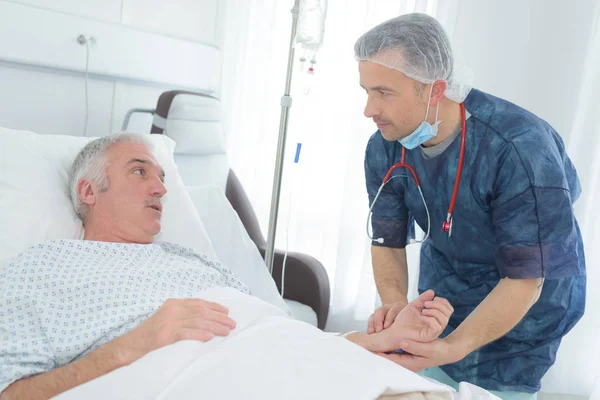 Дружній чоловік лікар тримає руку пацієнта в лікарняній кімнаті — стокове фото