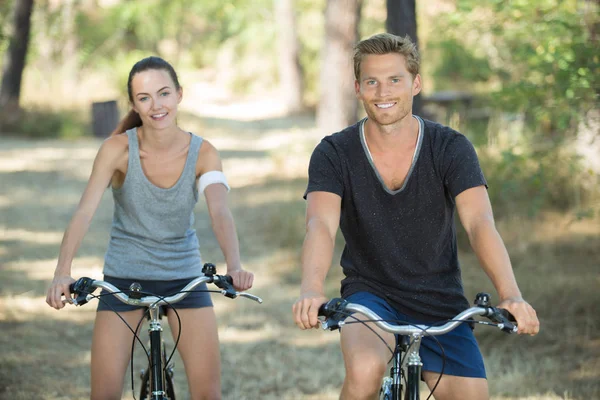 Couple sportif souriant faisant du vélo en forêt — Photo