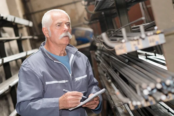 Senior werknemer tellen van metalen staven in magazijn — Stockfoto