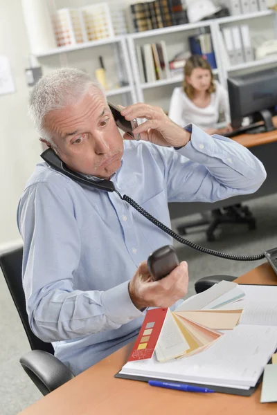 Homem na mesa segurando três telefones — Fotografia de Stock