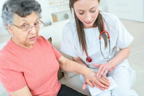 Kadın doktor krem üst düzey kadının elini koyarak — Stok fotoğraf