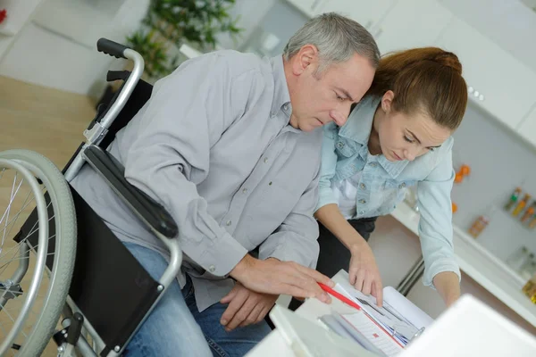 Jonge dame helpen midden leeftijd man in rolstoel — Stockfoto