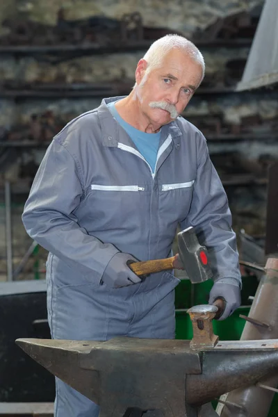 Старший кузнец обрабатывающий металл с молотком — стоковое фото