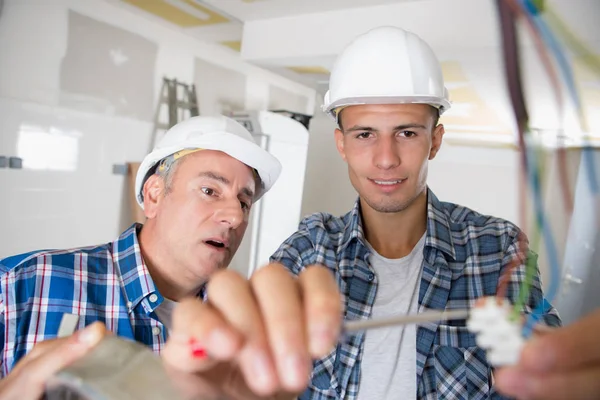 Friendly master electrician and apprentice working on breaker panel — Stock Photo, Image