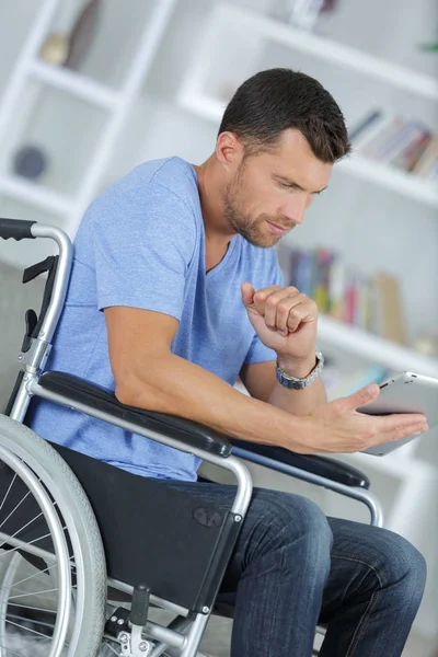 Homem com deficiência em cadeira de rodas usando tablet digital em casa — Fotografia de Stock