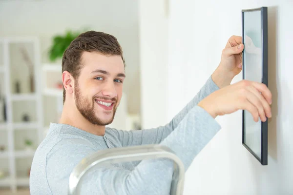 Happy man positioning picture frame on wall — Stock Photo, Image