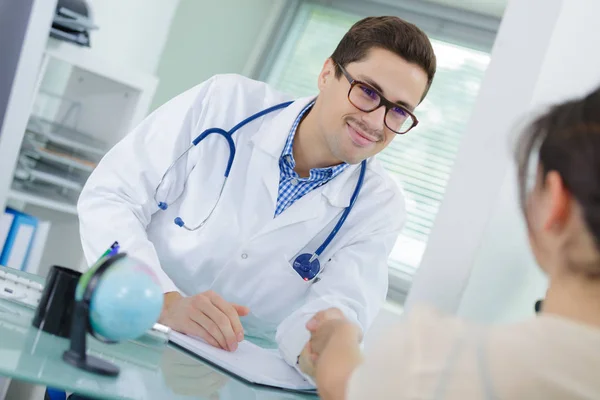 Joven médico saludando paciente con apretón de manos en su consultorio —  Fotos de Stock