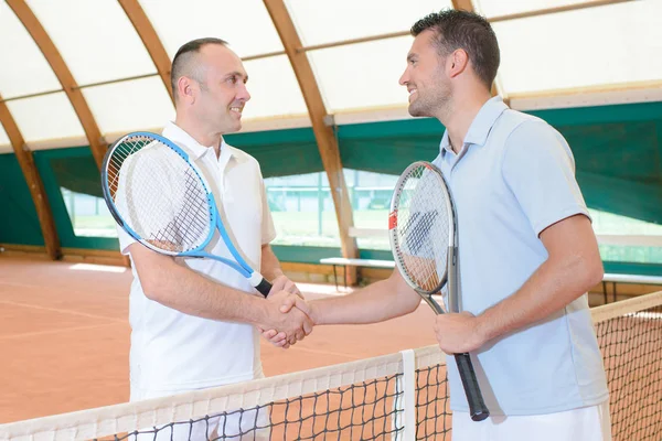 Dois homens apertando as mãos sobre a rede de quadra de tênis — Fotografia de Stock