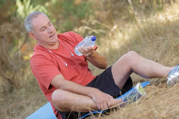 公園で座っていると水のボトルを保持している年配の男性 — ストック写真