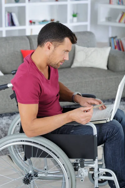 Ανάπηρο άνθρωπο σε αναπηρικό καροτσάκι, χρησιμοποιώντας φορητό υπολογιστή στο σπίτι — Φωτογραφία Αρχείου
