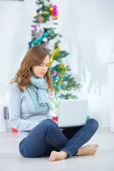Weibchen nutzt Computer neben Weihnachtsbaum zu Hause — Stockfoto