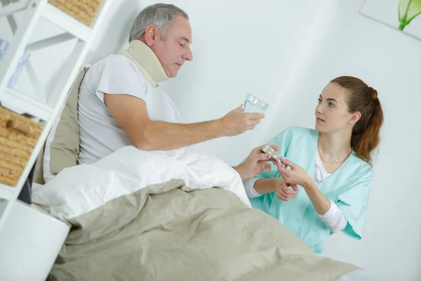 Zorgzame verpleegster helpen van zieke man om te drinken in bed — Stockfoto