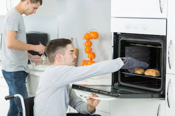 Behinderter junger Mann im Rollstuhl öffnet den Ofen — Stockfoto