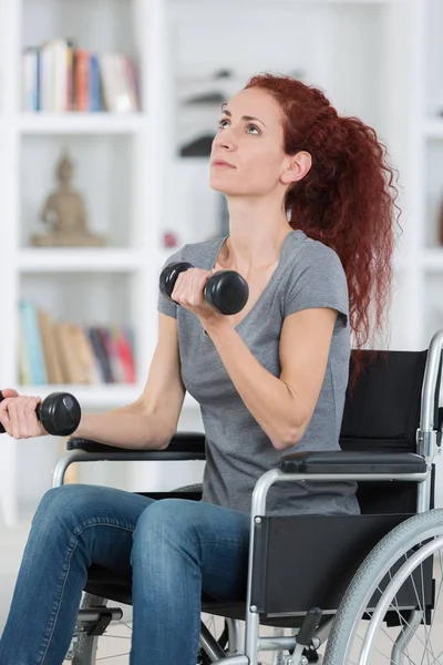 Femme assise en fauteuil roulant travaillant avec des haltères — Photo