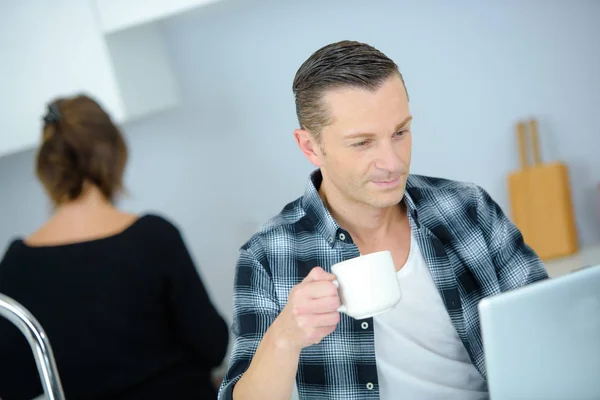 Empreendedor de boa aparência trabalhando no laptop enquanto toma café e café da manhã — Fotografia de Stock
