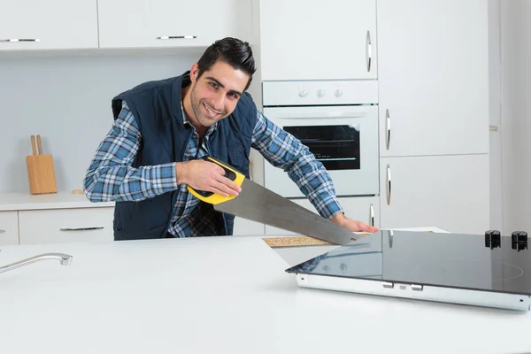 Carpenter using a hand saw in a kitchen — Stock Photo, Image