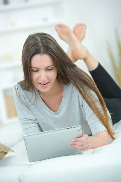 Attraente giovane donna con tablet digitale sul divano di casa — Foto Stock